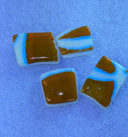 Four square glass art pieces with brown, light blue, and white marbled patterns, arranged on a textured blue surface.
